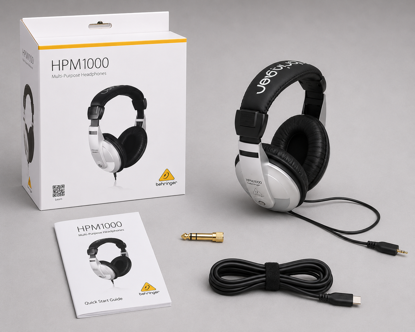 Behringer HPM1000 headphones shown with their product packaging, quick start guide, audio cable, and adapter.