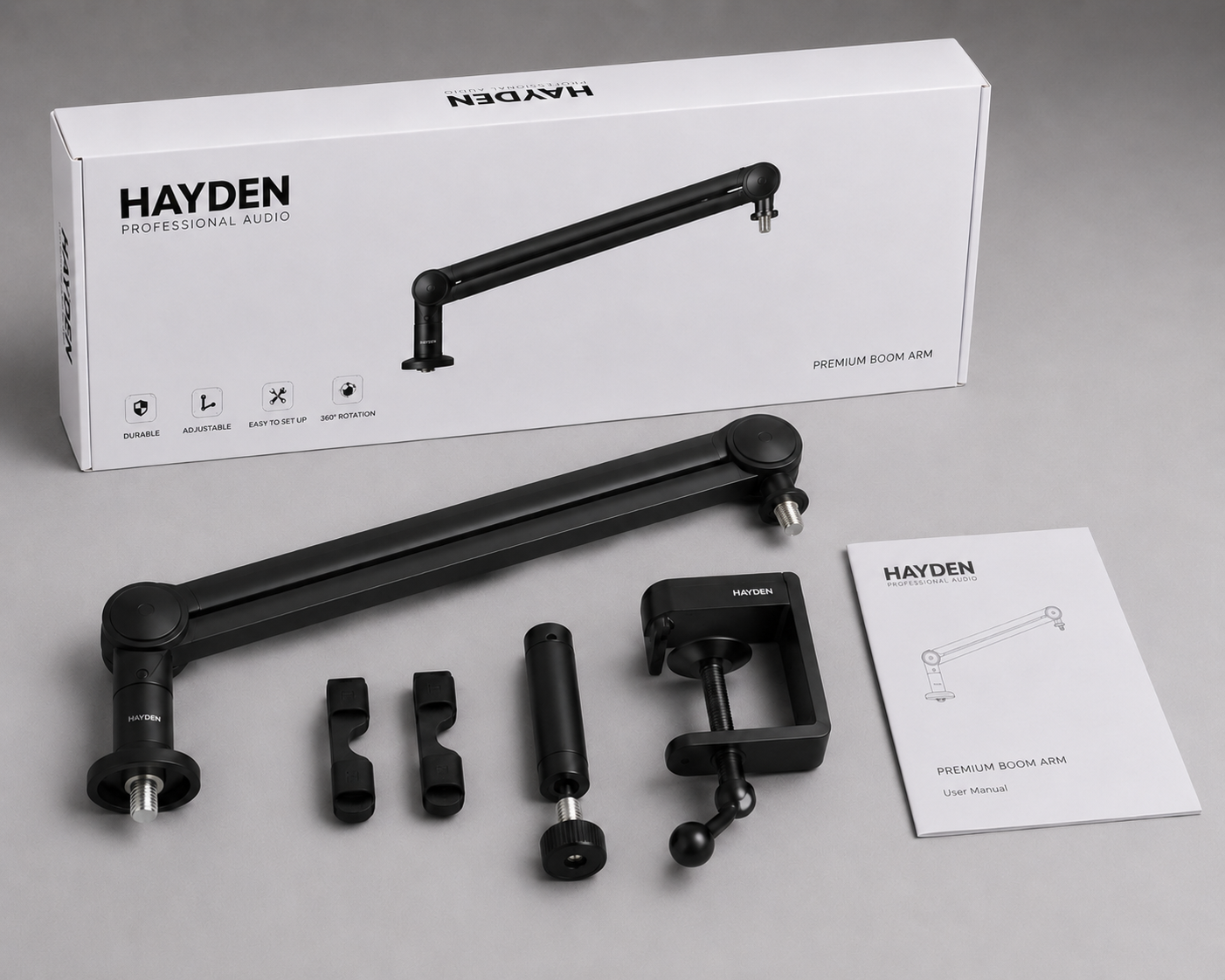 Hayden premium boom arm shown unboxed with its desk clamp, mounting accessories, user manual, and original box.